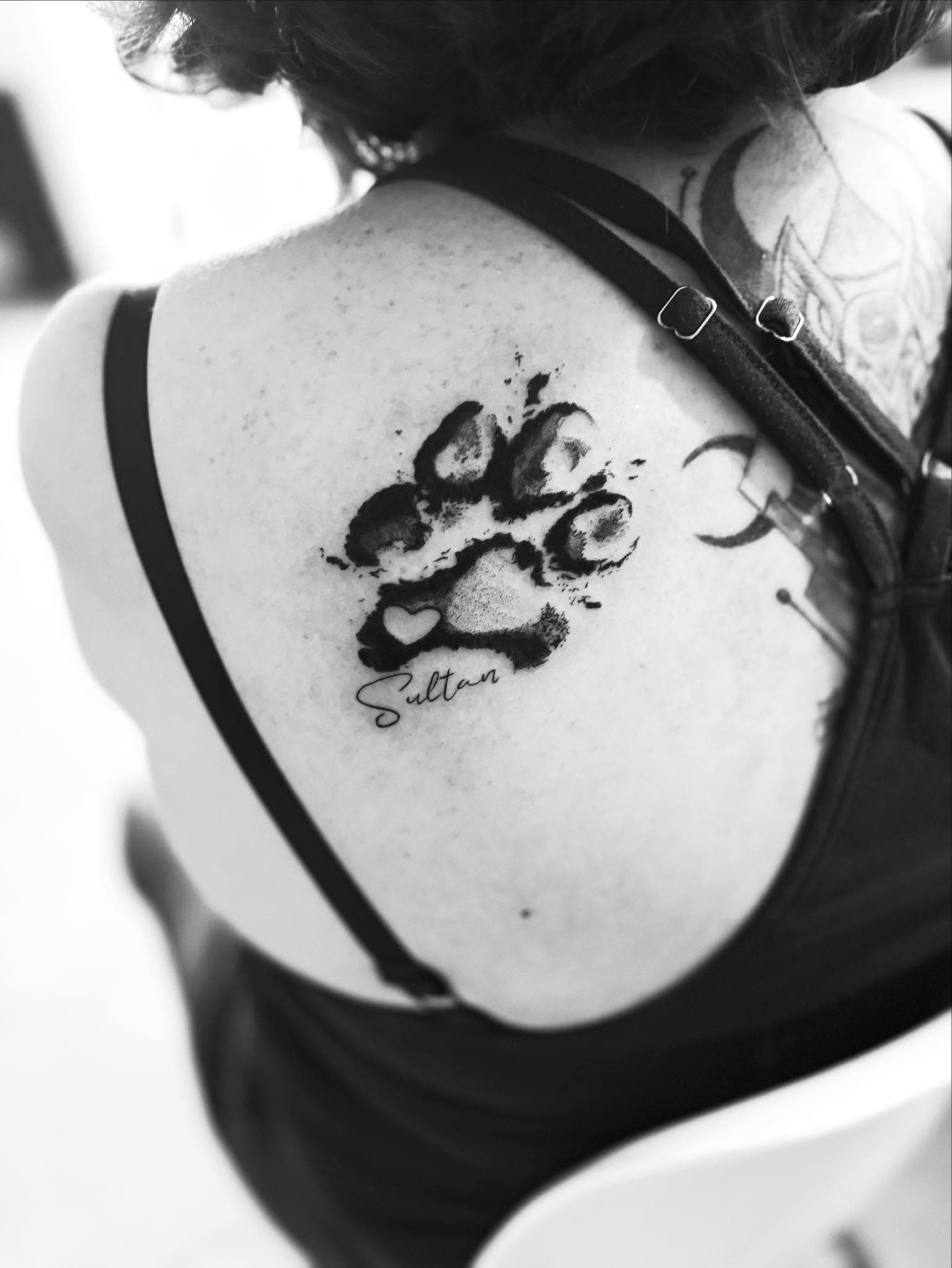 Tatouage fine line : empreinte de patte avec cœur et prénom Sultan sur l’omoplate