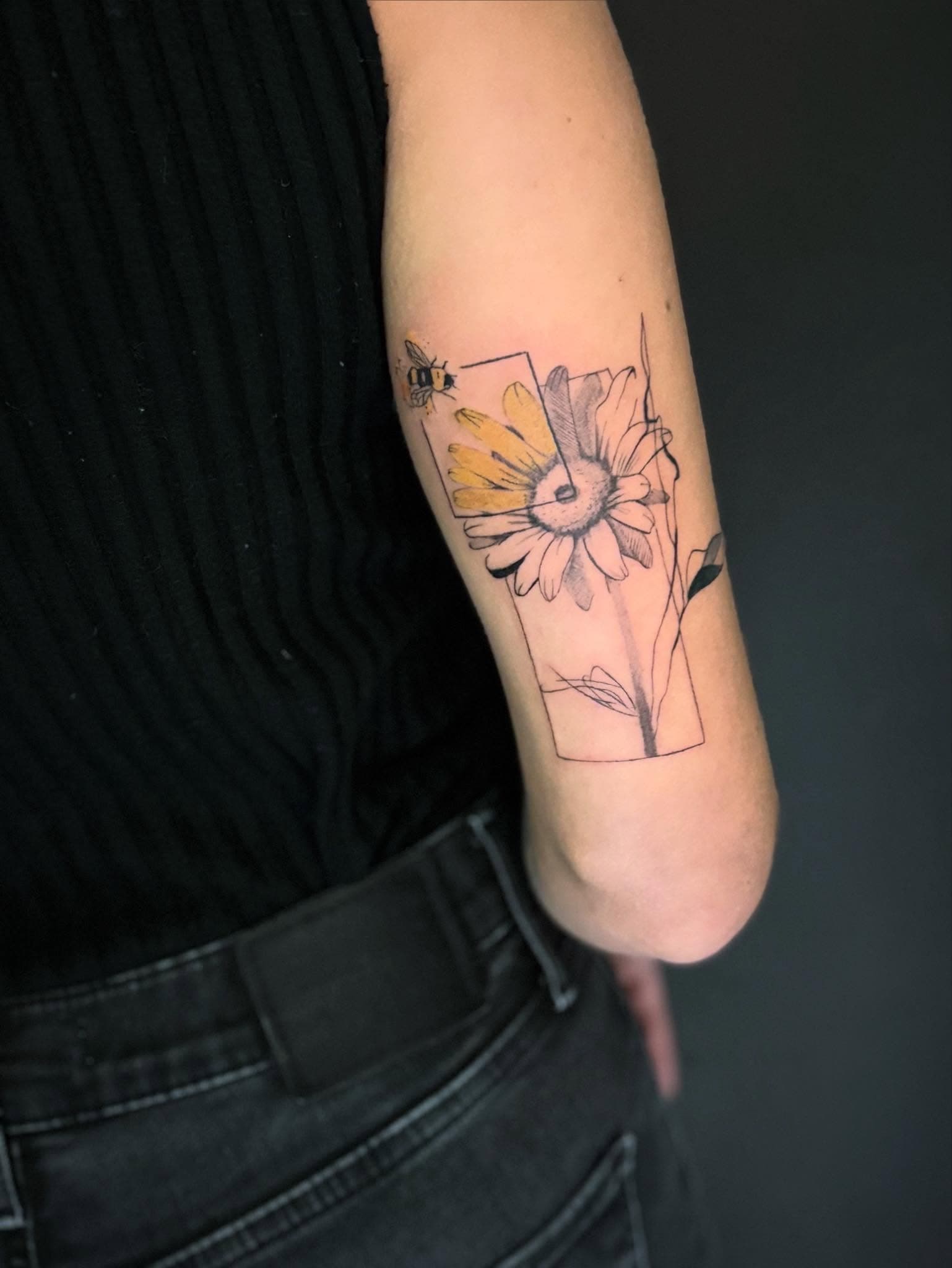 Tatouage fine line et micro-réalisme : marguerite et abeille avec accents jaunes sur le bras