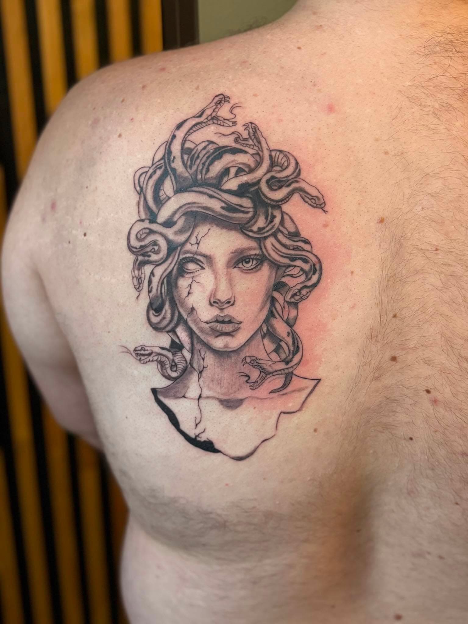 Tatouage micro-réalisme fine line : buste de Méduse en pierre sur le haut du dos