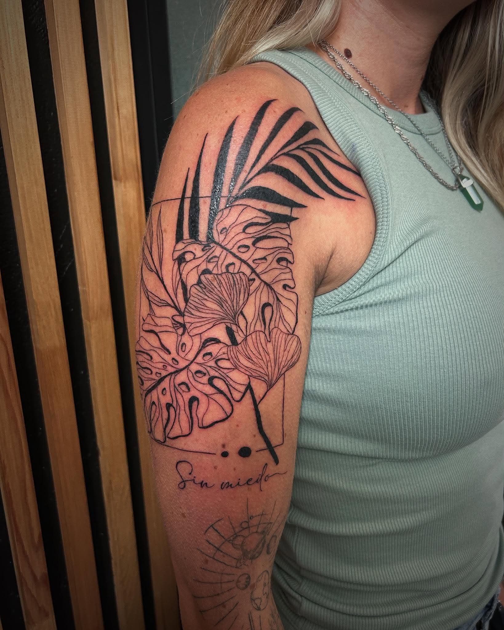Tatouage fine line botanique : palmier, monstera, ginkgo et inscription Sin miedo sur le bras
