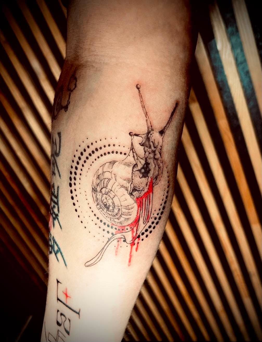 Tatouage fine line : escargot détaillé avec cercles géométriques en pointillés sur l’avant-bras