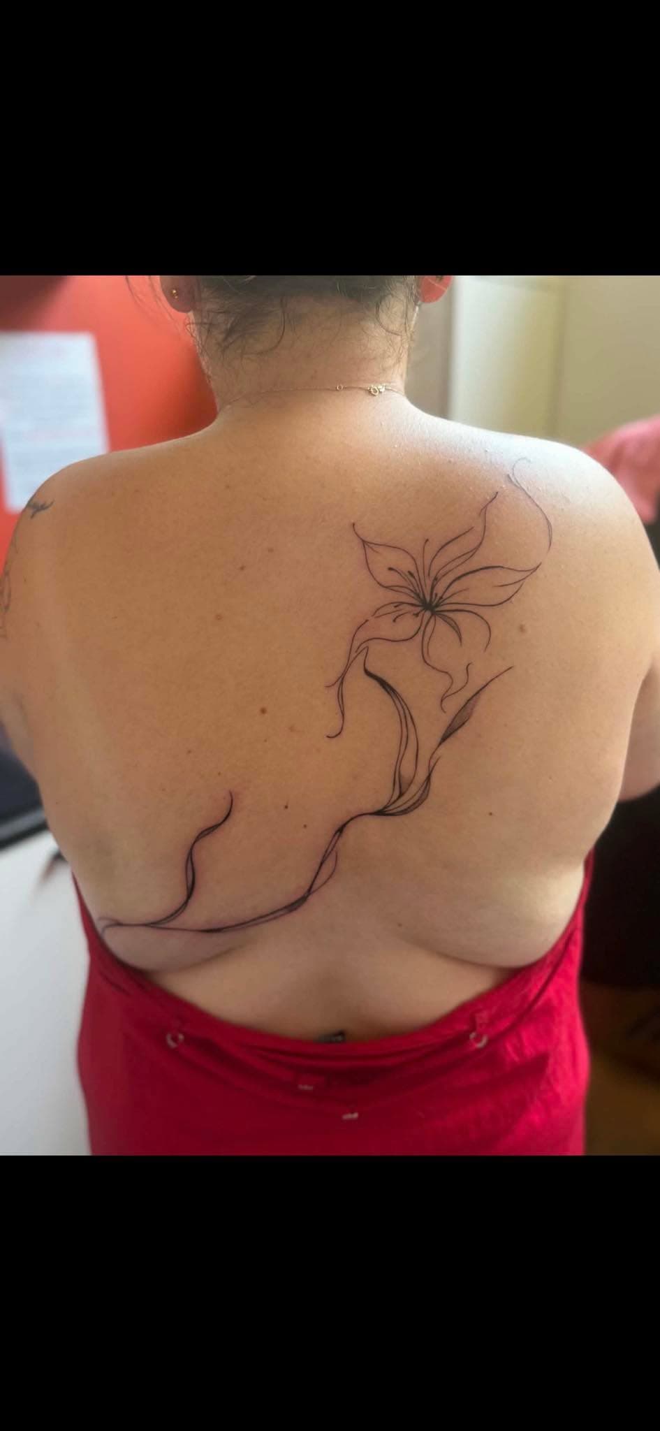 Tatouage fine line : fleur de lys avec tige courbe sur le dos