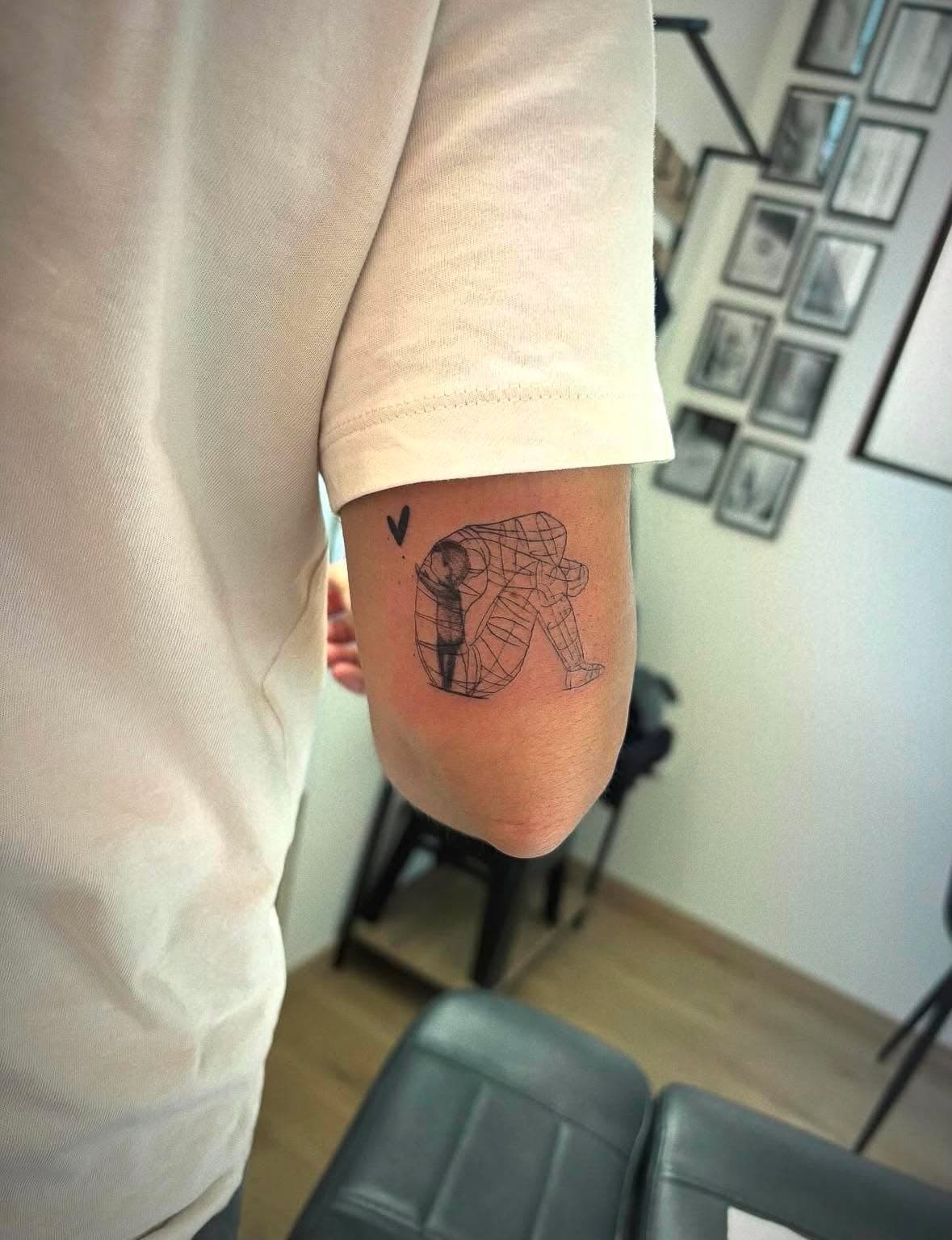 Tatouage fine line conceptuel : silhouette fil de fer avec enfant à l’intérieur sur le bras